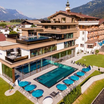 Urlaub in Söll mit Kindern oder als Pärchen Moderner Wellnessbereich mit Pool und blauen Sonnenschirmen an einem Hotel in den Bergen