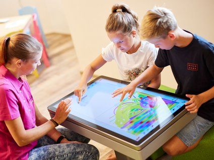 Spaß und Action im Kinderhotel in Söll Zwei Kinder und eine Erwachsene zeichnen an einem großen Touchscreen-Tisch