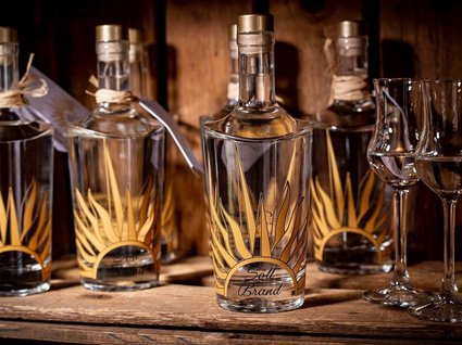 Kulinarische Verführungen in unserem Hotel in Söll/Tirol Flaschen mit klarem Likör und zwei gefüllte Schnapsgläser auf Holzregal