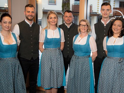 Arbeiten im Postwirt Gruppe von sechs Personen in traditioneller Trachtenkleidung vor Fenstern