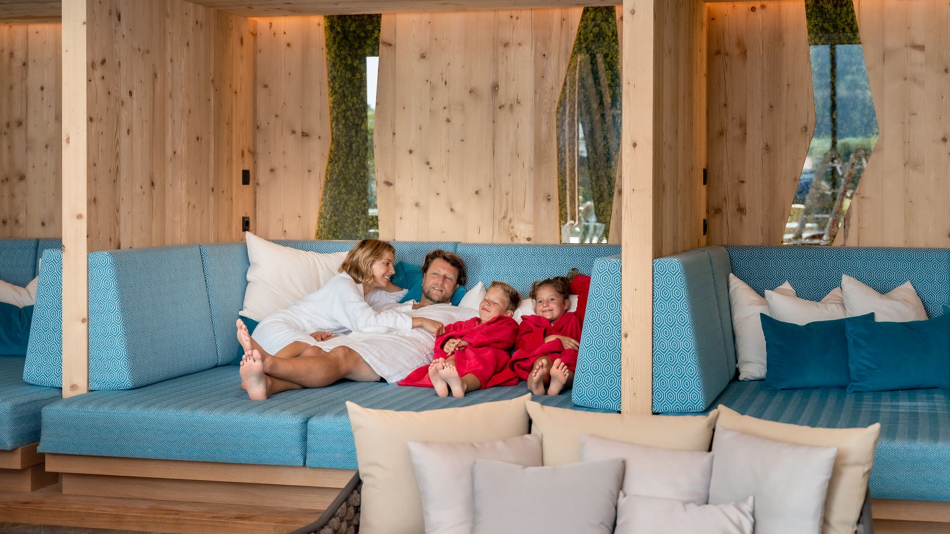 Familienhotel in Söll: der Postwirt Familie entspannt in Bademänteln auf blauem Sofa in modernem Holzzimmer