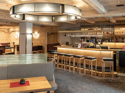 Kulinarische Verführungen in unserem Hotel in Söll/Tirol Gemütliche Bar mit Holzvertäfelung und hohen Holzstühlen an der Theke.