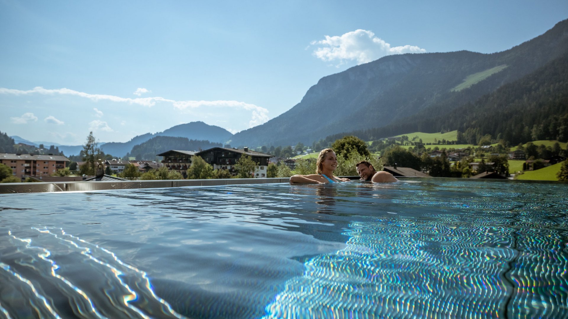 Hotel in Söll am Wilden Kaiser: der Postwirt Paar entspannt im Infinity-Pool mit Bergblick bei sonnigem Wetter