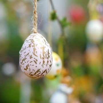 Urlaub in Söll mit Kindern oder als Pärchen Dekoratives Osterei mit goldenen Mustern an Schnur aufgehängt vor unscharfem Hintergrund