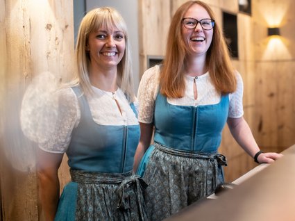 Arbeiten im Postwirt Zwei lächelnde Frauen in traditionellen Trachten an einem Holztresen
