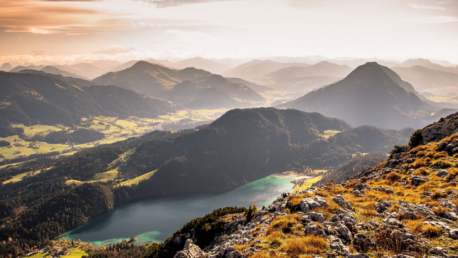 Entdecken Sie die Region mit der Wilder Kaiser GästeCard! Herbstliche Berglandschaft mit See und felsigem Vordergrund in warmem Licht
