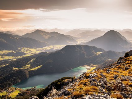 Entdecken Sie die Region mit der Wilder Kaiser GästeCard! Herbstliche Berglandschaft mit See und felsigem Vordergrund in warmem Licht