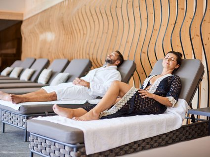 Paar entspannt auf Spa-Liegen Ein Paar in Bademänteln entspannt auf bequemen Liegen im Spa-Bereich, umgeben von einem modernen Holzdesign.