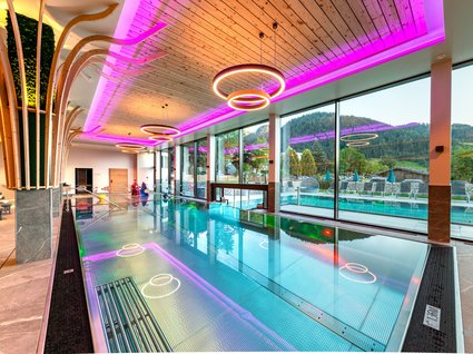 Ihre Traumtage im Postwirt Söll Moderner Innenpool mit großer Glasfront und lila Deckenbeleuchtung