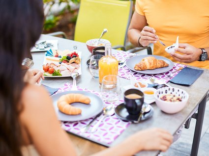 Ihre Traumtage im Postwirt Söll Zwei Personen frühstücken draußen mit Croissants, Aufschnitt, Kaffee und Orangensaft