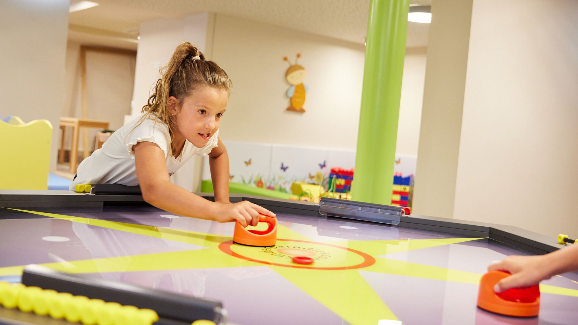 Spaß und Action im Kinderhotel in Söll Mädchen spielt Airhockey in einem Spielzimmer mit bunten Wänden