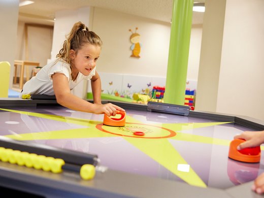 Mädchen spielt Airhockey im Spielbereich Ein Mädchen konzentriert sich beim Spielen von Airhockey in einem bunt gestalteten Indoor-Spielbereich eines Hotels.