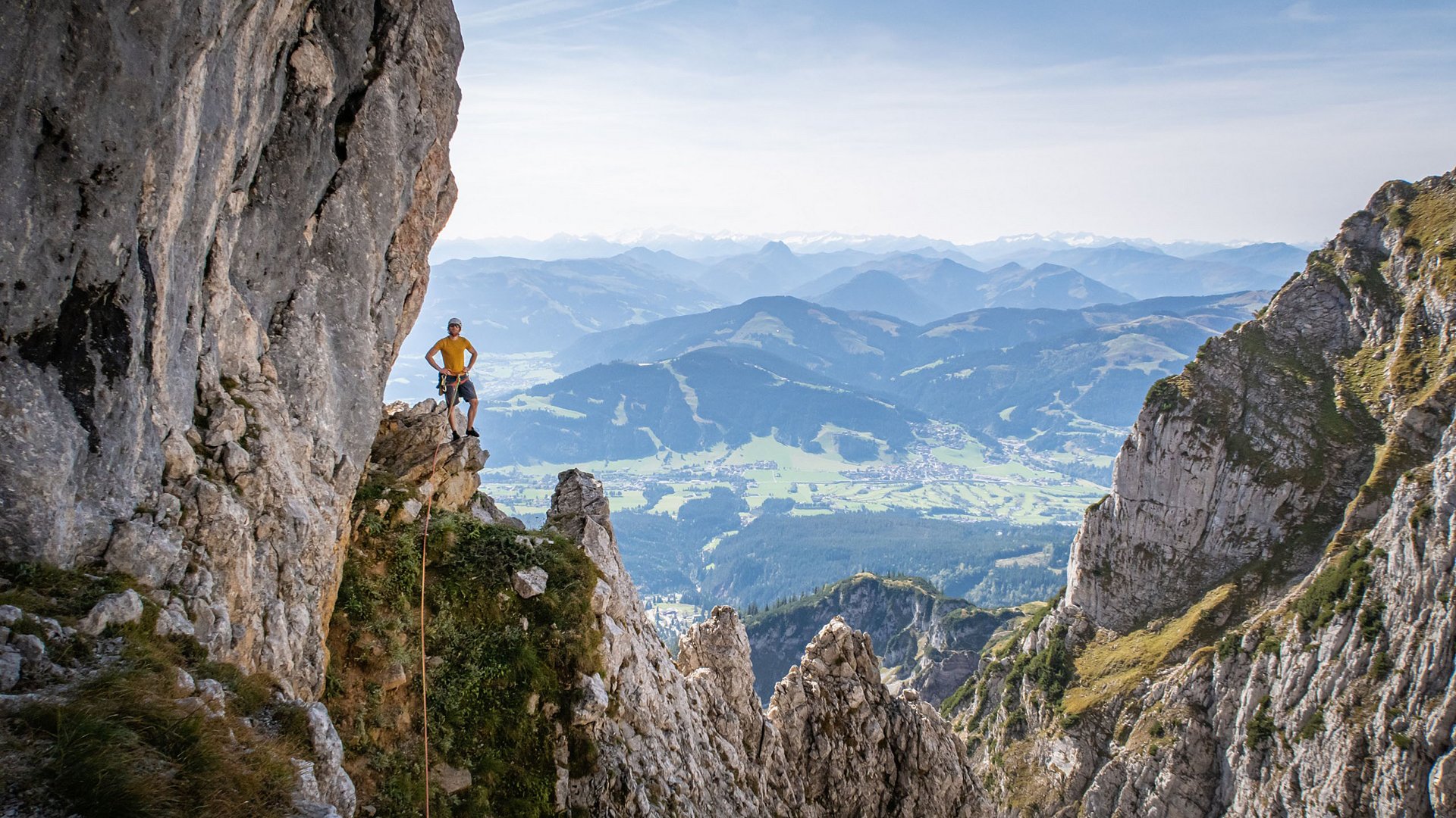 Entdecken Sie die Region mit der Wilder Kaiser GästeCard! Kletterer auf Felsvorsprung mit Panoramablick auf Berge und Tal