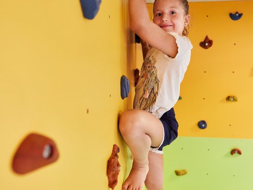 Hochwertige Ausstattung im Familienhotel am Wilden Kaiser Kind klettert an einer bunten Kletterwand mit Griffen im Innenbereich