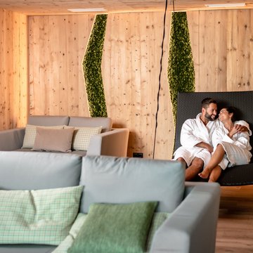 Urlaub in Söll mit Kindern oder als Pärchen Paar in Bademänteln entspannt auf Liege in modernem Holz- und Moos-Spa-Raum