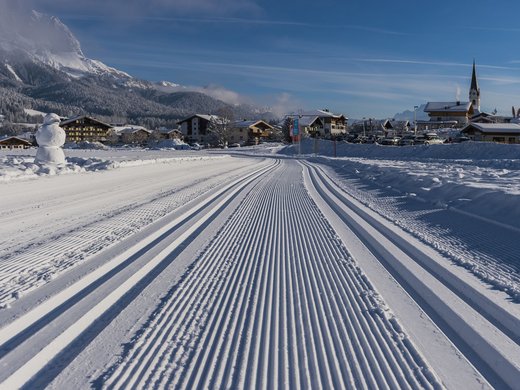 Winter in Söll: das Skigebiet SkiWelt Wilder Kaiser Gespurte Langlaufloipe vor verschneiten Bergen und einem Dorf bei klarem Himmel