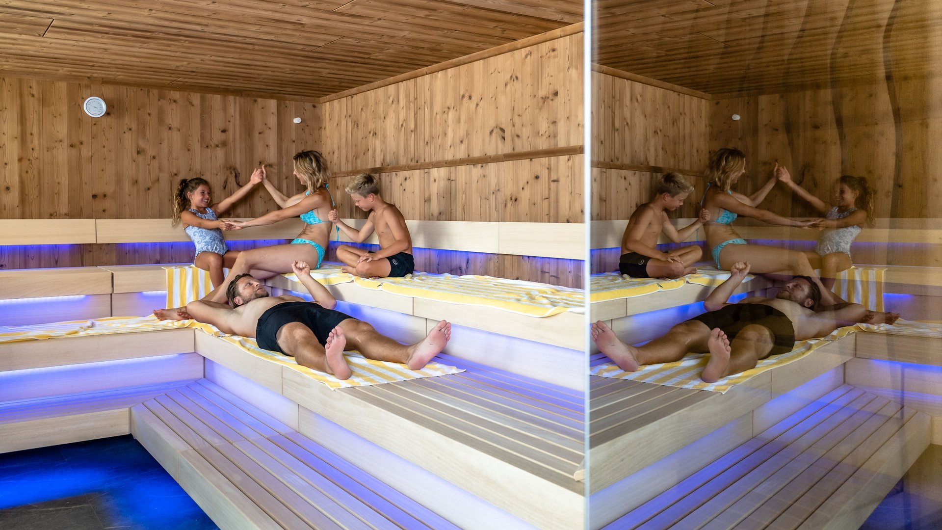 Familienhotel in Söll: der Postwirt Familie mit zwei Kindern entspannt zusammen in einer Sauna mit Holzwänden und blauer Beleuchtung