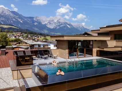 Der Postwirt: Hotel mit Infinitypool in Tirol Zwei Personen genießen einen Dachpool mit Bergblick und Sonnenliegen im Hintergrund
